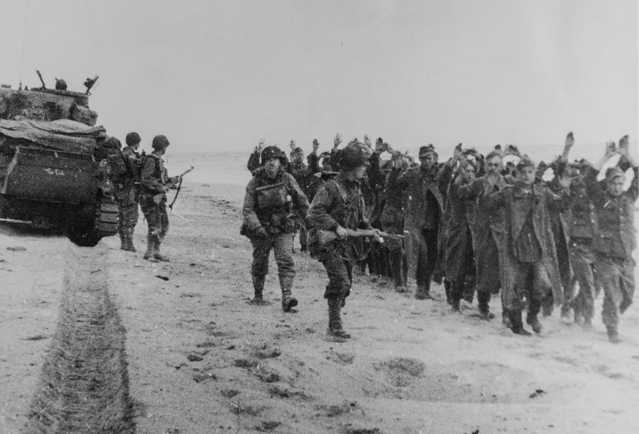 Original Caption: American soldiers march a group of German prisoners along a beachhead in Northern France after which they will be sent to England. June 6, 1944.