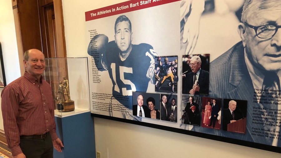 Athletes in Action President Mark Householder standing next to the Bart Starr Award at AIA headquarters in Xenia, Ohio.